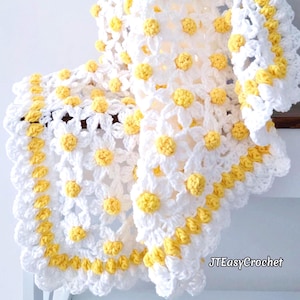 May include: A white crochet blanket with a daisy design, featuring yellow centres. The blanket has a scalloped edge with yellow detailing. The text "JTEasyCrochet" is visible in the bottom right corner.