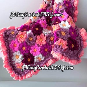 Pode incluir: Um cobertor de beb&eacute; em croch&ecirc; com um design floral em tons de rosa, roxo e branco. O cobertor tem uma borda festonada e o texto "JTEasyCrochet.ETSY.com" &eacute; vis&iacute;vel na imagem.