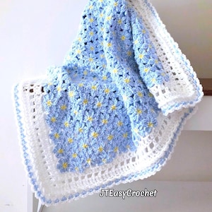 May include: A handmade crochet blanket featuring a repeating pattern of light blue flowers with bright yellow centers. The blanket is finished with a wide, white, open-weave border and a light blue scalloped edge. Text reads JTEasyCrochet.