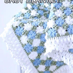 Lavishly beautiful crochet floral blanket made of cornflower motifs is hanging from a display. The blanket resembles a field of white and blue cornflowers framed with a beautiful lace edging.  The lettering says "Cornflowers Baby Blanket", "Crochet Pattern By JTEasyCrochet" meaning that JTEasyCrochet has the best crochet patterns for flower baby blankets, throws and afghans.