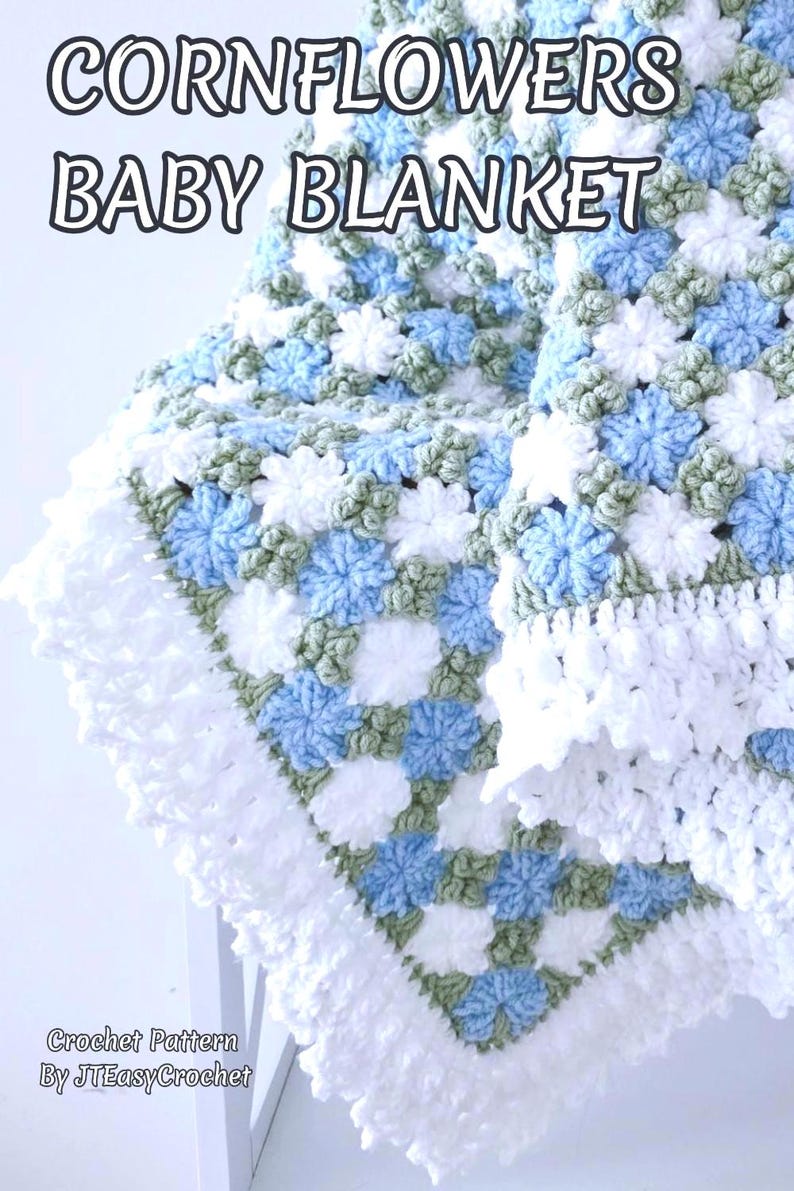 Lavishly beautiful crochet floral blanket made of cornflower motifs is hanging from a display. The blanket resembles a field of white and blue cornflowers framed with a beautiful lace edging.  The lettering says "Cornflowers Baby Blanket", "Crochet Pattern By JTEasyCrochet" meaning that JTEasyCrochet has the best crochet patterns for flower baby blankets, throws and afghans.