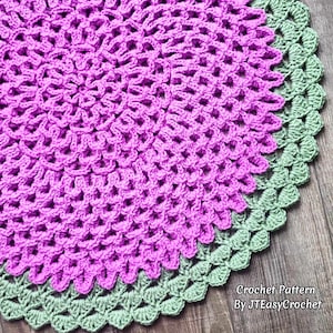 May include: A handmade, round crochet item with a vibrant purple center and a sage green scalloped edge. The crochet pattern is visible, creating a textured surface. The text "Crochet Pattern By JTEasyCrochet" is in the lower right corner.