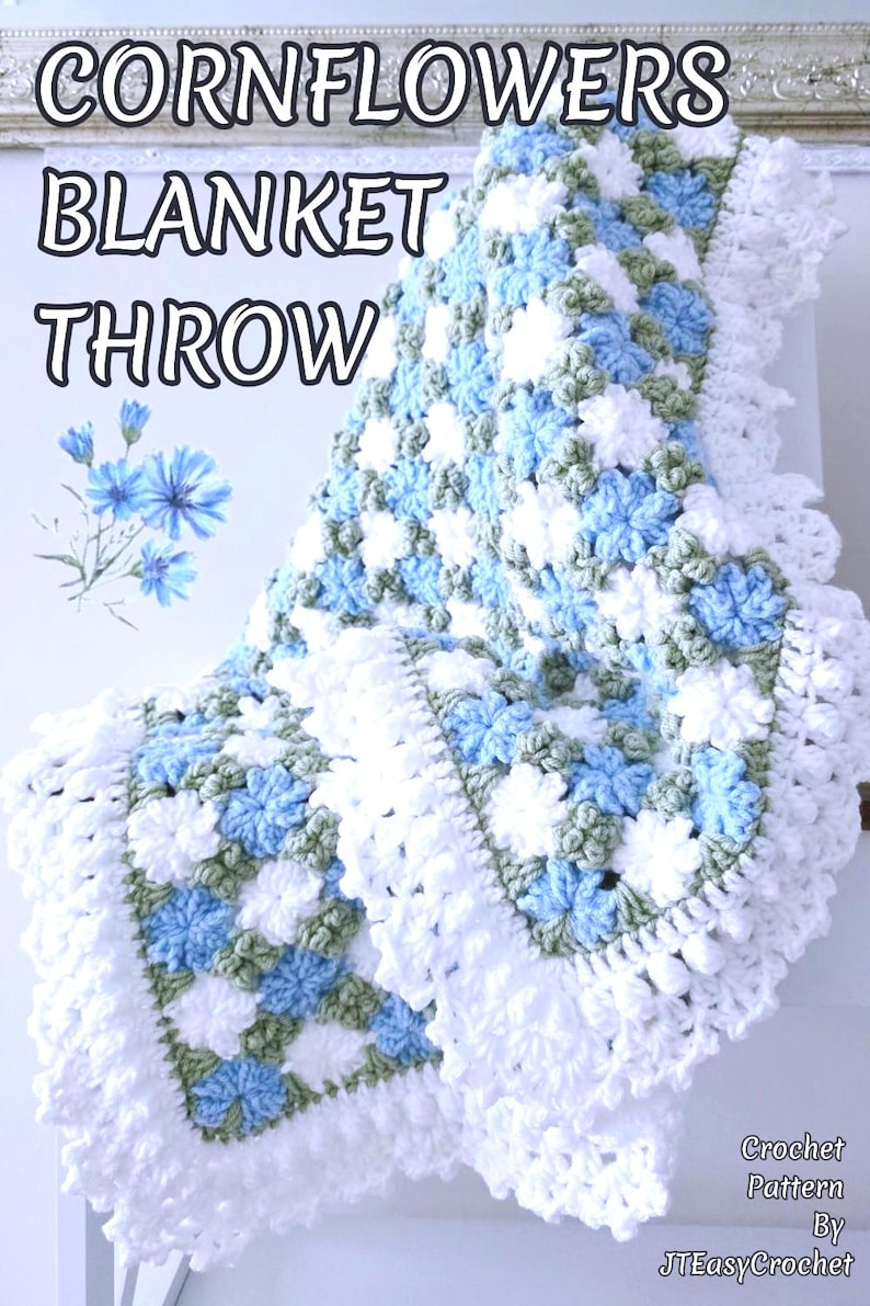 Lavishly beautiful crochet floral blanket made of cornflower motifs is hanging from a display. The blanket resembles a field of white and blue cornflowers framed with a beautiful lace edging.  The lettering says "Cornflowers Blanket Throw", "Crochet Pattern By JTEasyCrochet" meaning that JTEasyCrochet has the best crochet patterns for flower baby blankets, throws and afghans.