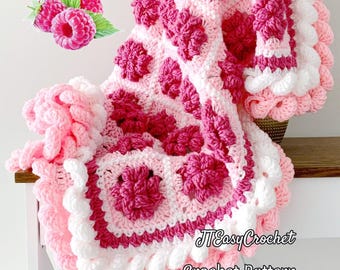 May include: A handmade crochet blanket in shades of pink and white, featuring a floral pattern. The blanket has a scalloped edge and the text "JTEasyCrochet Crochet Pattern" is visible. The blanket is folded over a white surface.