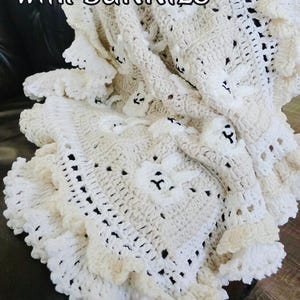 Beautiful Bunny  granny square blanket with fringed edging is laying on a dark leather couch. The blanket is cream with white bunnies on each square. The lettering says: “Baby Blanket With Bunnies”, “Crochet Pattern By JTEasyCrochet” meaning that JTEasyCrochet has the best crochet patterns and fun crochet ideas.