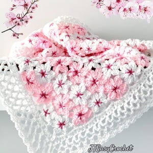 May include: A handmade crochet blanket in white, pink, and red. The blanket features a floral pattern with a white openwork border. The text "JTEasyCrochet" is visible in the lower right corner. Cherry blossom branches are in the background.