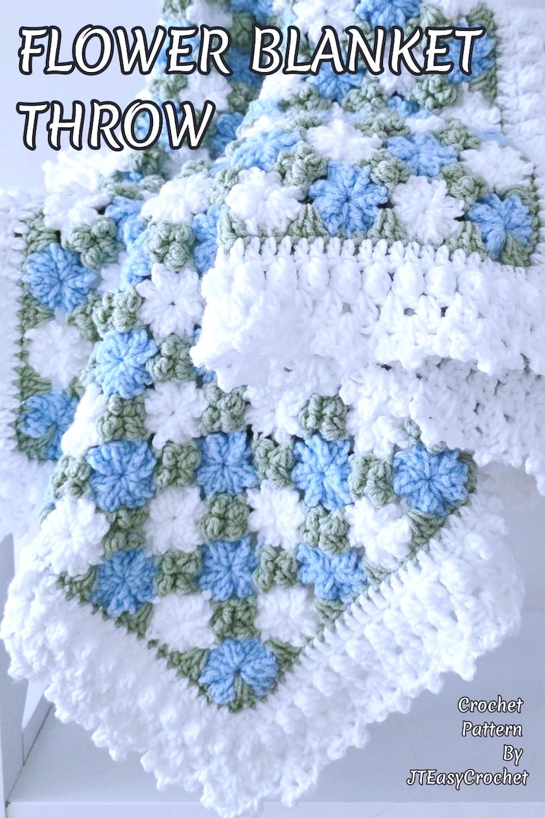 Lavishly beautiful crochet floral blanket made of cornflower motifs is hanging from a display. The blanket resembles a field of white and blue cornflowers framed with a beautiful lace edging.  The lettering says "Cornflowers Baby Blanket", "Crochet Pattern By JTEasyCrochet" meaning that JTEasyCrochet has the best crochet patterns for flower baby blankets, throws and afghans.