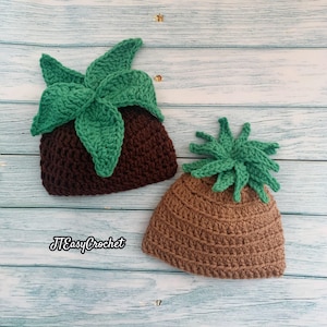 May include: Two handmade crochet hats, one resembling a brown pot with green leaves and the other a tan pineapple. The hats are displayed on a light blue wooden surface. The text "JTEasyCrochet" is visible.