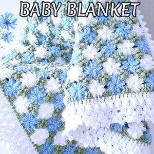 Lavishly beautiful crochet floral blanket made of cornflower motifs is hanging from a display. The blanket resembles a field of white and blue cornflowers framed with a beautiful lace edging.  The lettering says "Cornflowers Baby Blanket", "Crochet Pattern By JTEasyCrochet" meaning that JTEasyCrochet has the best crochet patterns for flower baby blankets, throws and afghans.