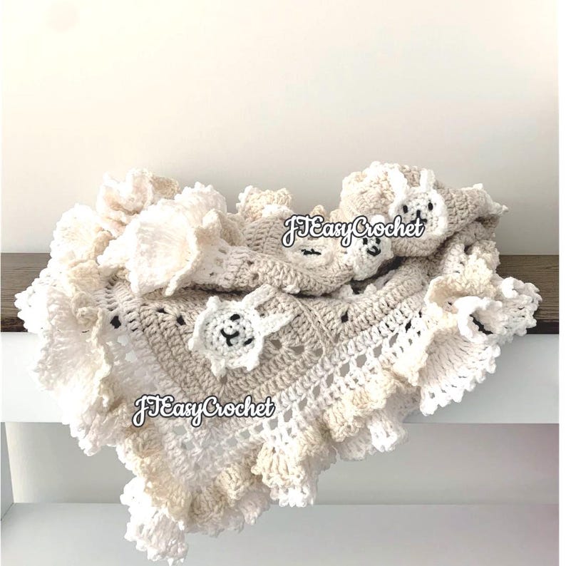 Op de afbeelding: Een gehaakt babydekentje in wit en beige met een gegolfde rand. Het dekentje heeft kleine gehaakte dierenapplicaties. Het dekentje is gelabeld met "JTEasyCrochet".