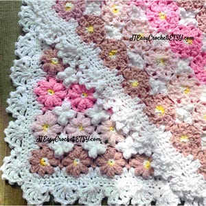 May include: A handmade crochet blanket featuring a floral pattern in shades of pink, white, and brown. The blanket has a scalloped edge and the text "JTEasyCrochetETSY.com" is visible. This cozy blanket is perfect for a baby or as a decorative throw.