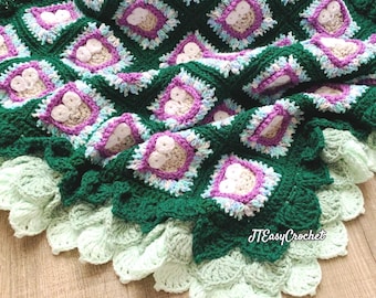 May include: A handmade crochet blanket in shades of green, white, and purple. The blanket features a repeating square pattern with floral-like designs in the center of each square. The border has a scalloped edge. The text "JTEasyCrochet" is visible.