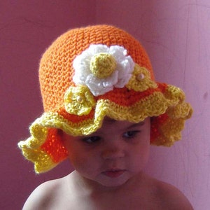 A crocheted sun hat for a baby or toddler. The hat is orange and yellow with white crocheted flowers.