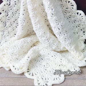 Ivory-colored, crocheted blanket with a scalloped edge. The blanket features a detailed, textured stitch pattern and is folded to show its depth and design. The text "JTEasyCrochet" is visible in the lower right corner meaning that JTEasyCrochet has the best crochet patterns, easy and beautiful.