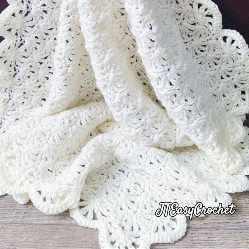 Ivory-colored, crocheted blanket with a scalloped edge. The blanket features a detailed, textured stitch pattern and is folded to show its depth and design. The text "JTEasyCrochet" is visible in the lower right corner meaning that JTEasyCrochet has the best crochet patterns, easy and beautiful.