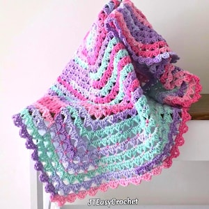 May include: A handmade crochet blanket featuring a repeating shell stitch pattern in a variegated color palette of soft lavender, bright pink, and light mint green. The textile has a scalloped edge and the text JTEasyCrochet is printed at the bottom.