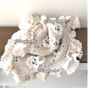 Op de afbeelding: Een wit en cr&egrave;mekleurig gehaakt babydekentje met een gegolfde rand en kleine gehaakte schapenapplicaties. Het dekentje is gevouwen en heeft de tekst "JJ Easy Crochet" erop.