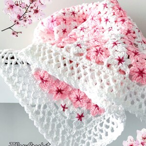 May include: A white and pink crocheted blanket with a floral pattern. The blanket features a repeating design of pink flowers with dark pink centers. The words "JTEasyCrochet" are in the lower left corner.