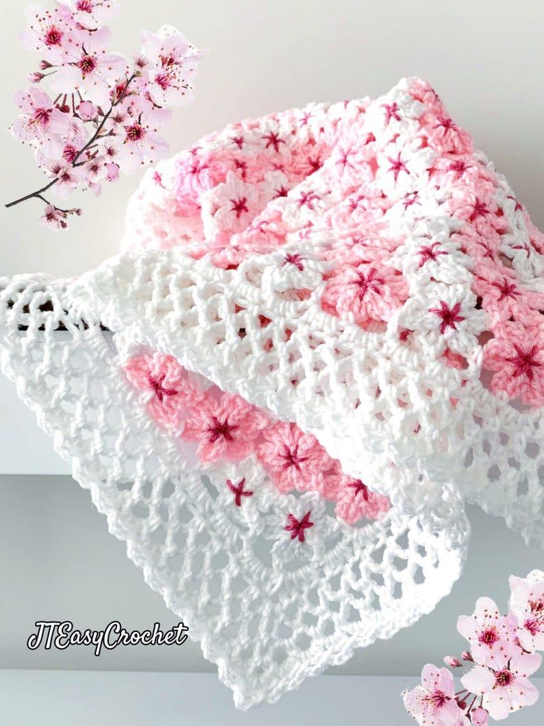 May include: A white and pink crocheted blanket with a floral pattern. The blanket features a repeating design of pink flowers with dark pink centers. The words "JTEasyCrochet" are in the lower left corner.
