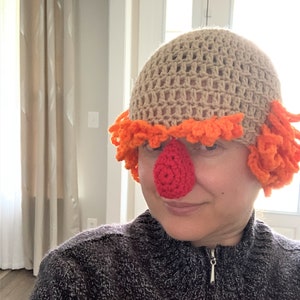 May include: A crocheted hat with orange and brown yarn, featuring a red crocheted nose. The hat has a loose, floppy style and is worn by a person.