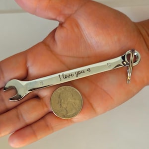 May include: A silver wrench keychain with the words "I love you" engraved on it. The keychain is shown with a quarter for size comparison. The wrench has a loop for attaching keys.