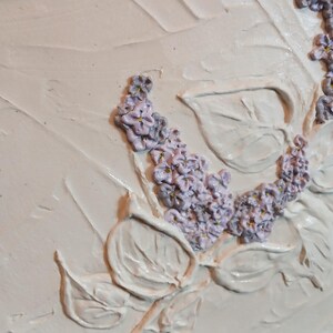 Könnte beinhalten: Strukturiertes Kunstwerk mit erhabenen, cremefarbenen Blättern und Lavendelblütenbüscheln. Das Stück ist in einem schwarzen Rahmen eingefasst und schafft ein dreidimensionales Blumendesign. Das Kunstwerk hat eine rustikale, handgefertigte Ästhetik.