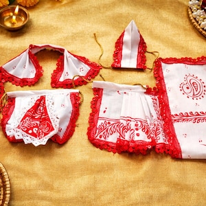 May include: White and red decorative fabric pieces with intricate patterns and lace trim. The set includes various shapes, possibly for ceremonial use, arranged on a golden surface. The pieces have red borders and designs.