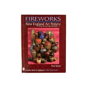 May include: A hardcover book titled FIREWORKS New England Art Pottery of the Arts & Crafts Movement by Paul Royka. The dark red cover features a central photograph displaying a collection of various ceramic vases and vessels in earthy tones.