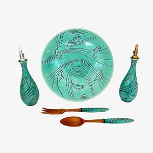 May include: A teal ceramic serving set with a fish design. The set includes a large plate, two bottles, a fork, and a spoon. The plate and bottles have a teal background with black fish illustrations. The wooden fork and spoon have teal accents.