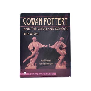 May include: A book titled "COWAN POTTERY AND THE CLEVELAND SCHOOL WITH VALUES" features two nude statues on the cover. The book is a Schiffer Book for Collectors, with the authors Mark Bassett and Victoria Naumann.