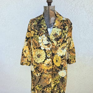 May include: A long-sleeved jacket featuring a bold floral pattern in shades of mustard yellow, golden brown, cream, and black. The garment has a notched lapel collar, a single-button front closure, and a straight hemline, displayed on a mannequin.