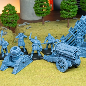 May include: A collection of blue miniature war machines and figurines. The set includes a mortar, a multi-barrel cannon, a rocket launcher, and several soldiers. The figures are posed as if in battle, set on a green surface.