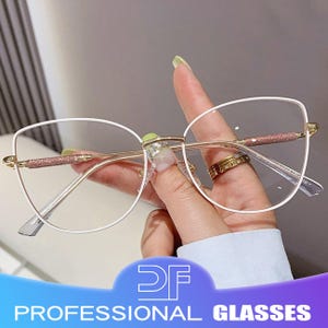 Op de afbeelding: Bril met witte montuur, gouden brug en veren. De veren hebben een glitterroze accent. De lenzen zijn helder. De tekst "DF PROFESSIONAL GLASSES" staat onderaan de afbeelding.