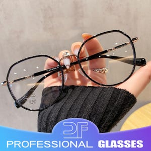 May include: Black-framed eyeglasses with a geometric design. The glasses have clear lenses and gold-colored accents on the bridge and temples. The text "PROFESSIONAL GLASSES" is visible at the bottom of the image.