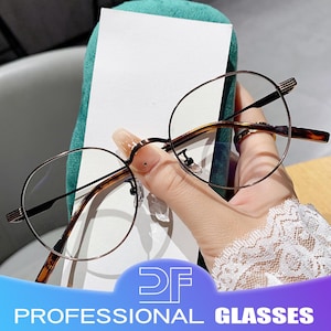 May include: Round-framed eyeglasses with a thin, dark metal frame and tortoise-shell arms. The glasses are held in a hand with long nails. The text "PROFESSIONAL GLASSES" is displayed in a blue and white banner.