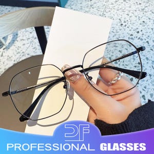 以下が含まれることがあります： 幾何学的な形状の黒いフレームの眼鏡。 眼鏡は透明なレンズで、白い背景に保持されています。 画像の下部には「PROFESSIONAL GLASSES」というテキストが表示されています。