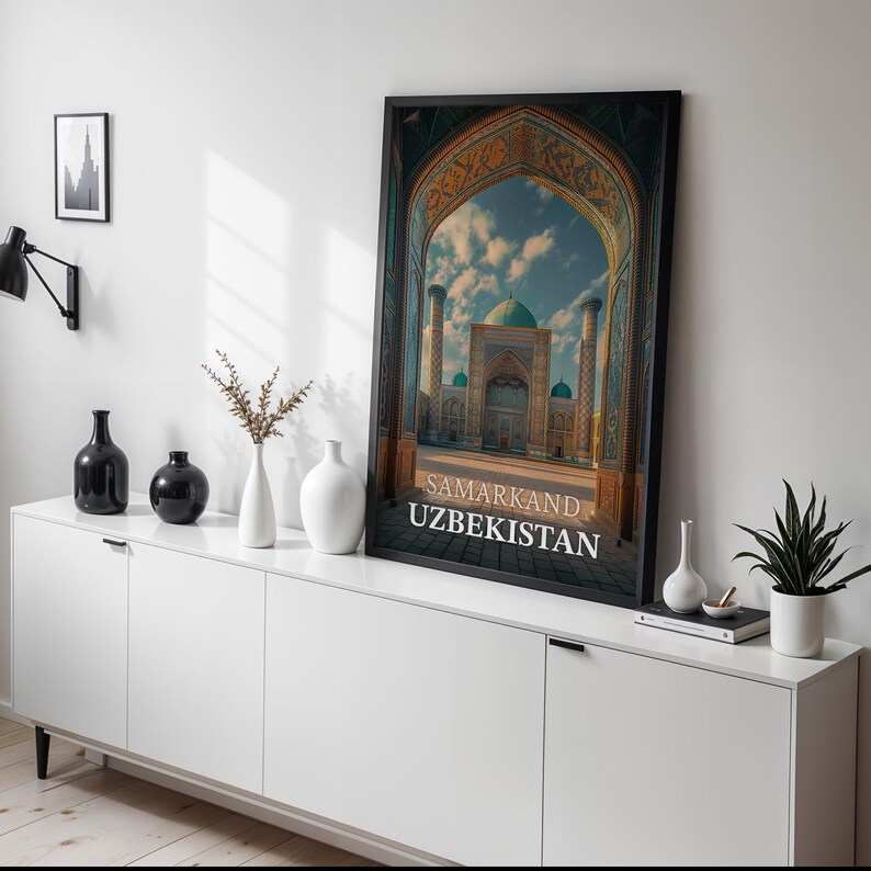 May include: A framed print of a building in Samarkand, Uzbekistan, with a large archway and turquoise domes. The print is displayed on a white cabinet with black vases and a small plant.