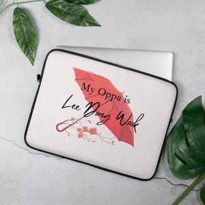 May include: White laptop sleeve featuring a red umbrella design with the text "My Oppa is Lee Dong Wook". The sleeve also includes a floral branch design. The sleeve has a black border.