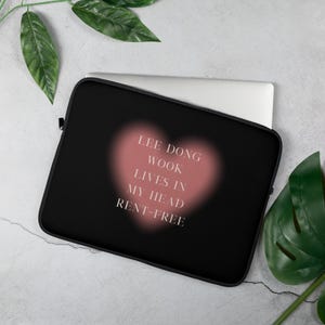 May include: Black laptop sleeve with the text "LEE DONG WOOK LIVES IN MY HEAD RENT-FREE" in white, set against a soft pink heart shape. The sleeve is designed to protect a laptop.