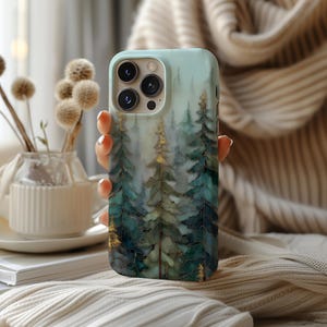May include: A mint green phone case featuring a watercolor forest scene with teal and gold accents. The case has a glossy finish and a camera cutout. The design includes tall evergreen trees and a misty background, creating a nature-inspired aesthetic.