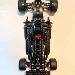 Puede incluir: Modelo de coche de carreras de Fórmula 1 negro con las palabras "PETRONAS" y "Syntium" impresas. El modelo tiene ruedas negras y un detalle rojo. El coche es una réplica detallada de un coche de carreras.