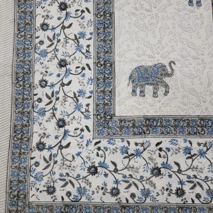 May include: A white fabric textile featuring a repeating pattern of blue and grey elephants, surrounded by a decorative border of blue and grey floral vines. The background includes a subtle, light grey paisley print across the main section.