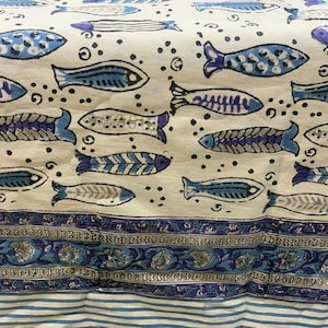 Peut inclure: Tissu crème avec un motif répété de poissons bleus de différentes formes. Le tissu présente également de petits points foncés et une bordure florale bleue sur le bord inférieur. Le bas est rayé bleu et blanc.