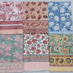 May include: Six folded fabric pieces with floral designs in various colours. The fabrics display patterns in pink, blue, green, and yellow, with detailed floral and geometric borders. These textiles are likely for home decor or crafting projects.