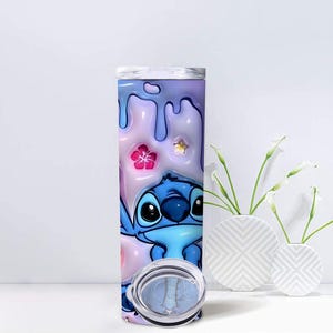May include: A tall, stainless steel tumbler featuring a cartoon character, Stitch, in shades of blue. The background has a pastel color scheme with dripping paint and floral accents. The tumbler includes a clear lid.