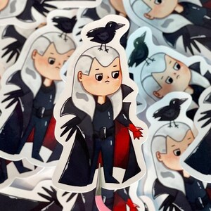 Puede incluir: Una colección de pegatinas con un personaje de dibujos animados con pelo blanco, un atuendo negro y una capa con forro rojo. Un cuervo negro está posado sobre la cabeza del personaje. Las pegatinas tienen un acabado brillante.