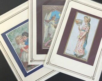 May include: Three framed vintage Christmas cards with illustrations of children. The first card features a boy and girl in Victorian clothing. The second card shows an angel with a star. The third card depicts a girl holding a fan with a Christmas message.