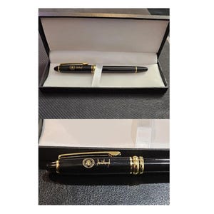 May include: A black pen with gold accents, presented in a black box with a white satin ribbon. The pen features a gold clip and a detailed emblem. The pen is a classic writing instrument, suitable for gifting or personal use.