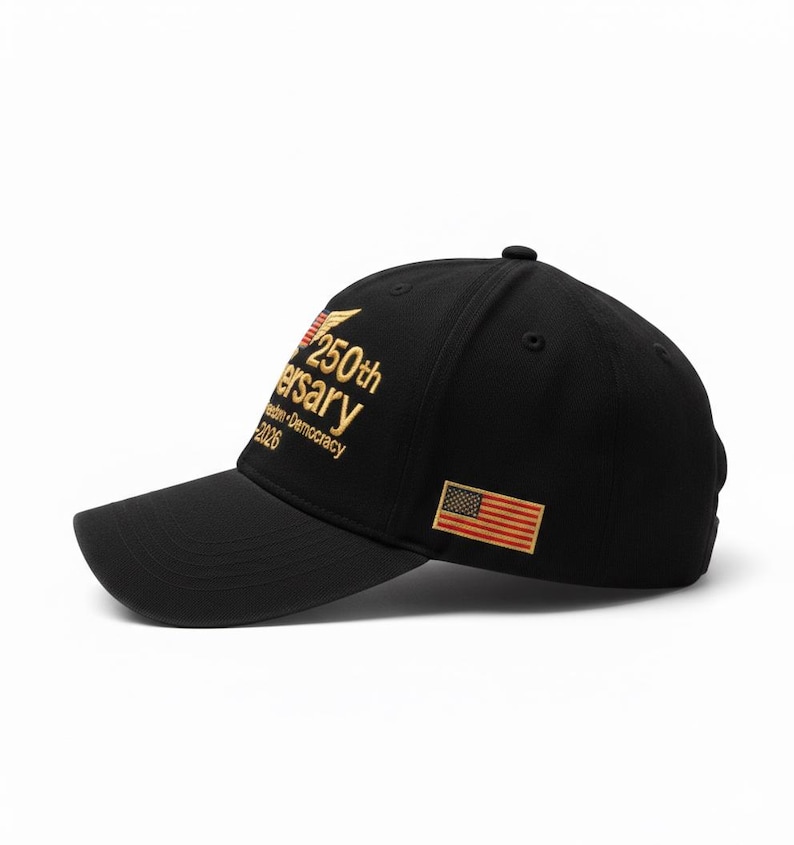 May include: Black baseball cap with a curved brim. Features gold embroidered text that reads "250th Anniversary Freedom Democracy 2026" and a small American flag patch. The cap is a classic style.