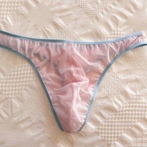 Puede incluir: Unos calzoncillos tipo bikini de color rosa claro semitransparente con un borde fino de color azul claro a lo largo de la cintura y las aberturas de las piernas. La tela es ligera y traslúcida, con un diseño frontal contorneado.
